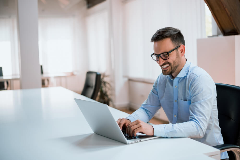 Smiling younger man sitting at modern desk using a laptop