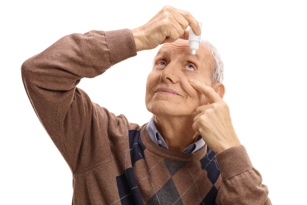 Older man putting eye drops in his eye to help treat glaucoma